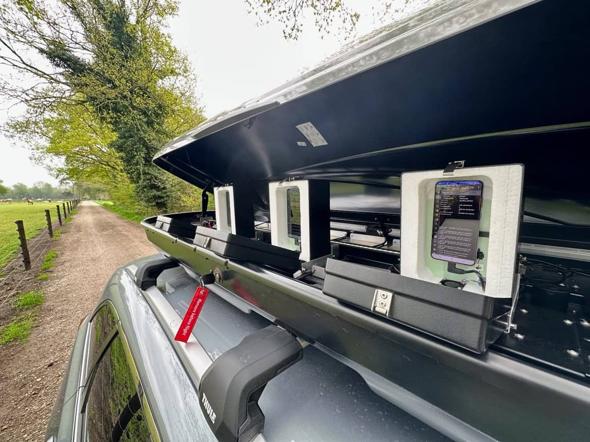 Groene auto met op het dak een dakkoffer met aan de zijkant een aantal mobiele telefoons