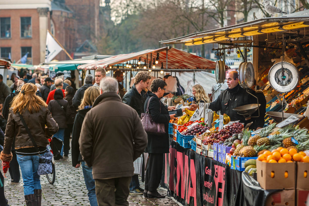 Klanten bij een groentenkraam. De marktkoopman weegt de groente af.