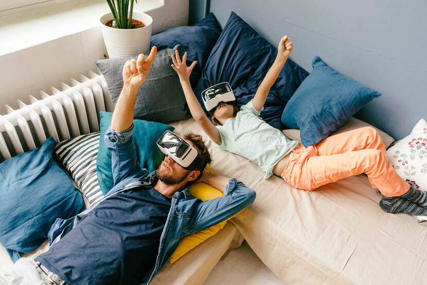 Man en klein meisje liggen met een VR bril op de bank te wijzen naar het plafond