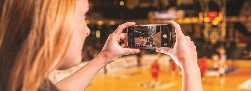 Vrouw met telefoon filmend tijdens een basketbalwedstrijd