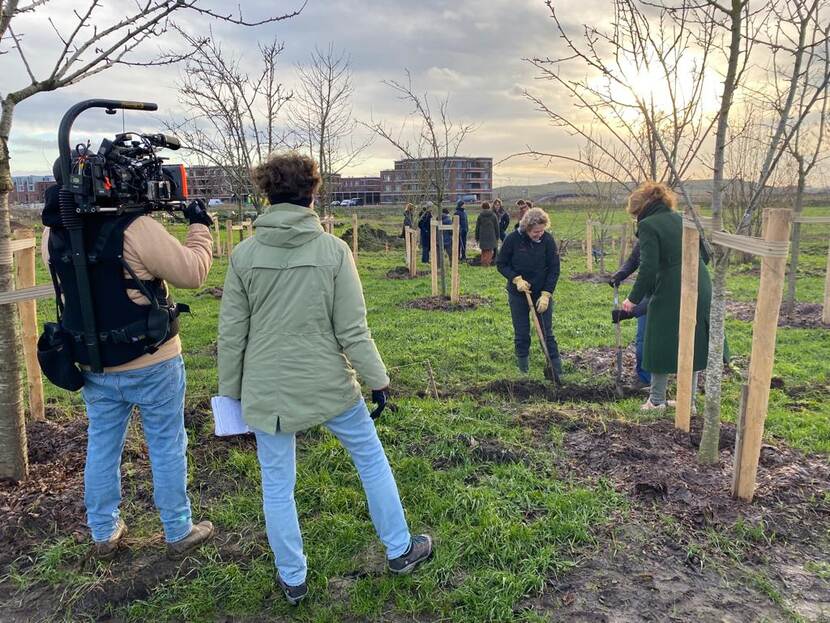 Mensen graven gaten om bomen in te planten. Een cameraploeg filmt dit.