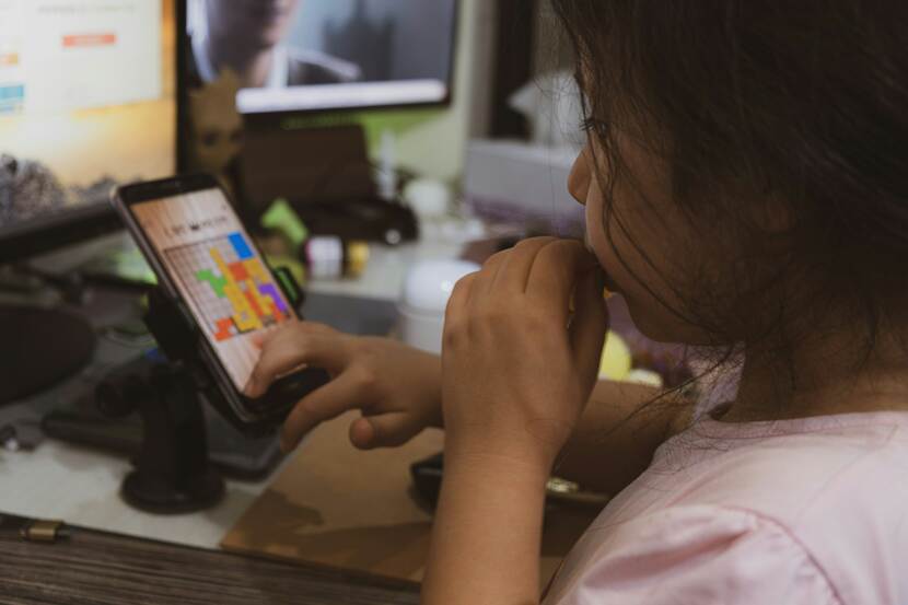Jong meisje zit aan tafel en speelt een spelletje op een smartphone